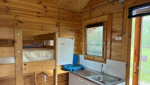 Una cabaña de madera compacta con literas, un kitchenette y una ventana con persianas.