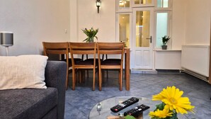 Un salon comprenant un canapé, une table à manger avec des chaises, une table basse en verre avec des télécommandes, et une porte dotée de panneaux en verre dépoli.