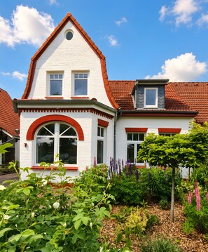 Ein zweistöckiges Haus mit rotem Ziegeldach, weißen Wänden und einem Garten mit verschiedenen Pflanzen.