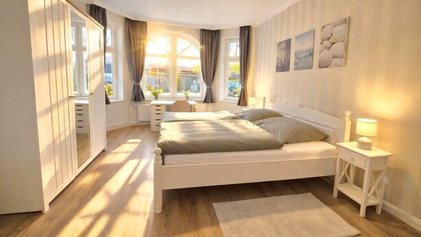 Une chambre à coucher comprenant un lit, une table de chevet, une lampe et une fenêtre donnant sur l’extérieur.