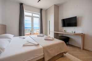 Une chambre d’hôtel avec un lit, un bureau, une télévision et une vue sur la mer.