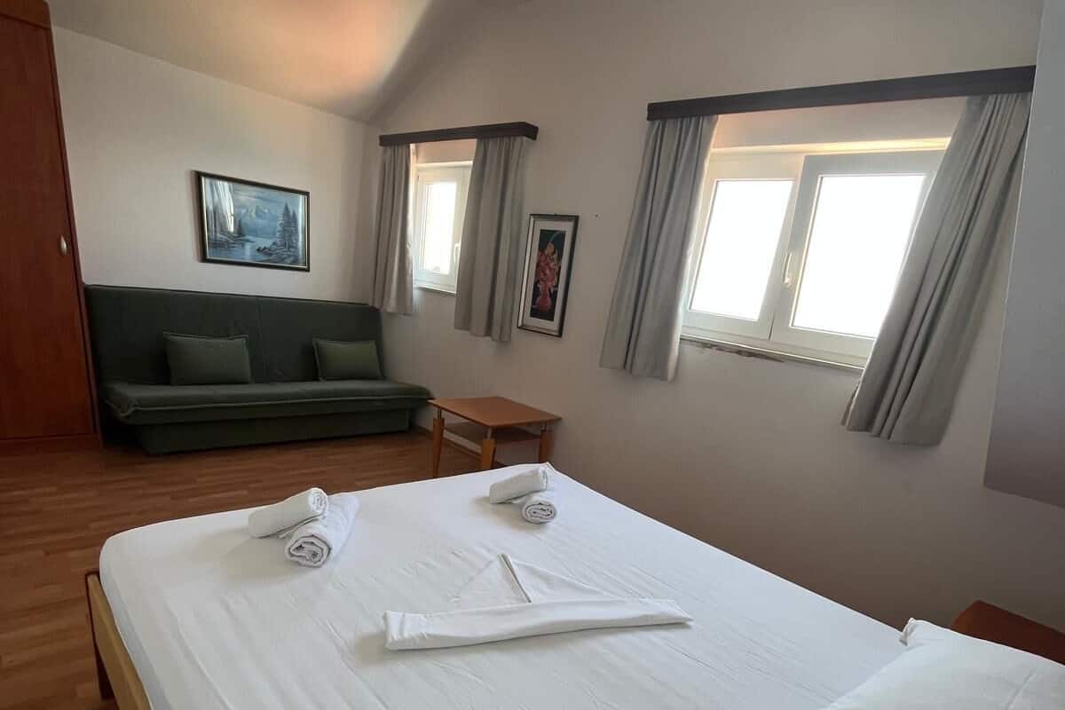 A hotel room with a bed, a sofa, a small table, and two windows with curtains.