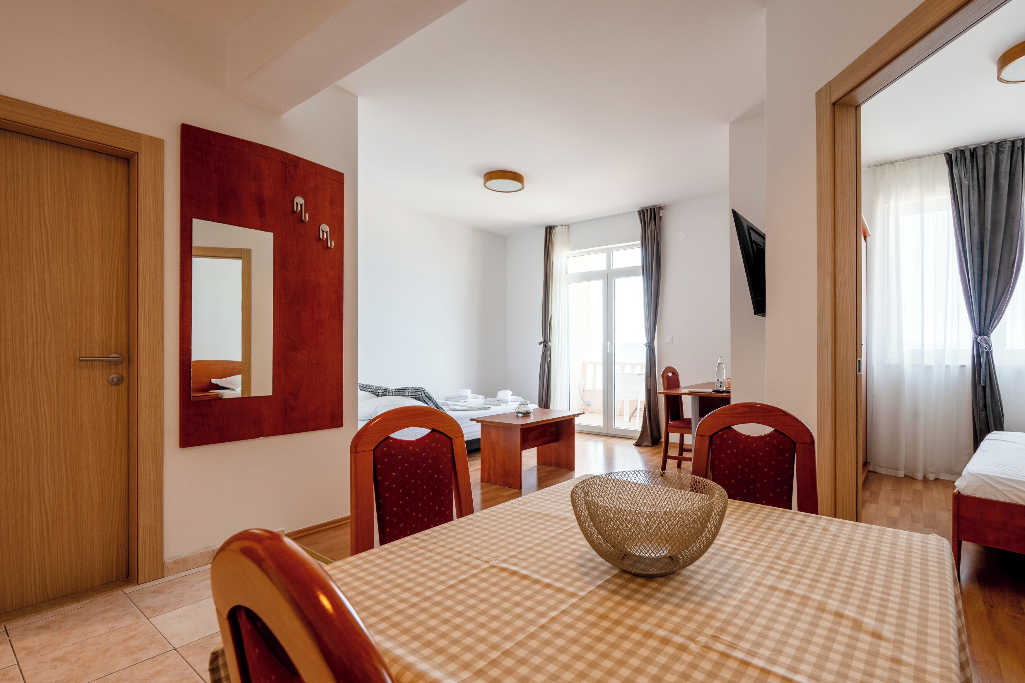 Une chambre d’hôtel avec une table à carreaux, un lit, un bureau, un miroir et un téléviseur fixé au mur.