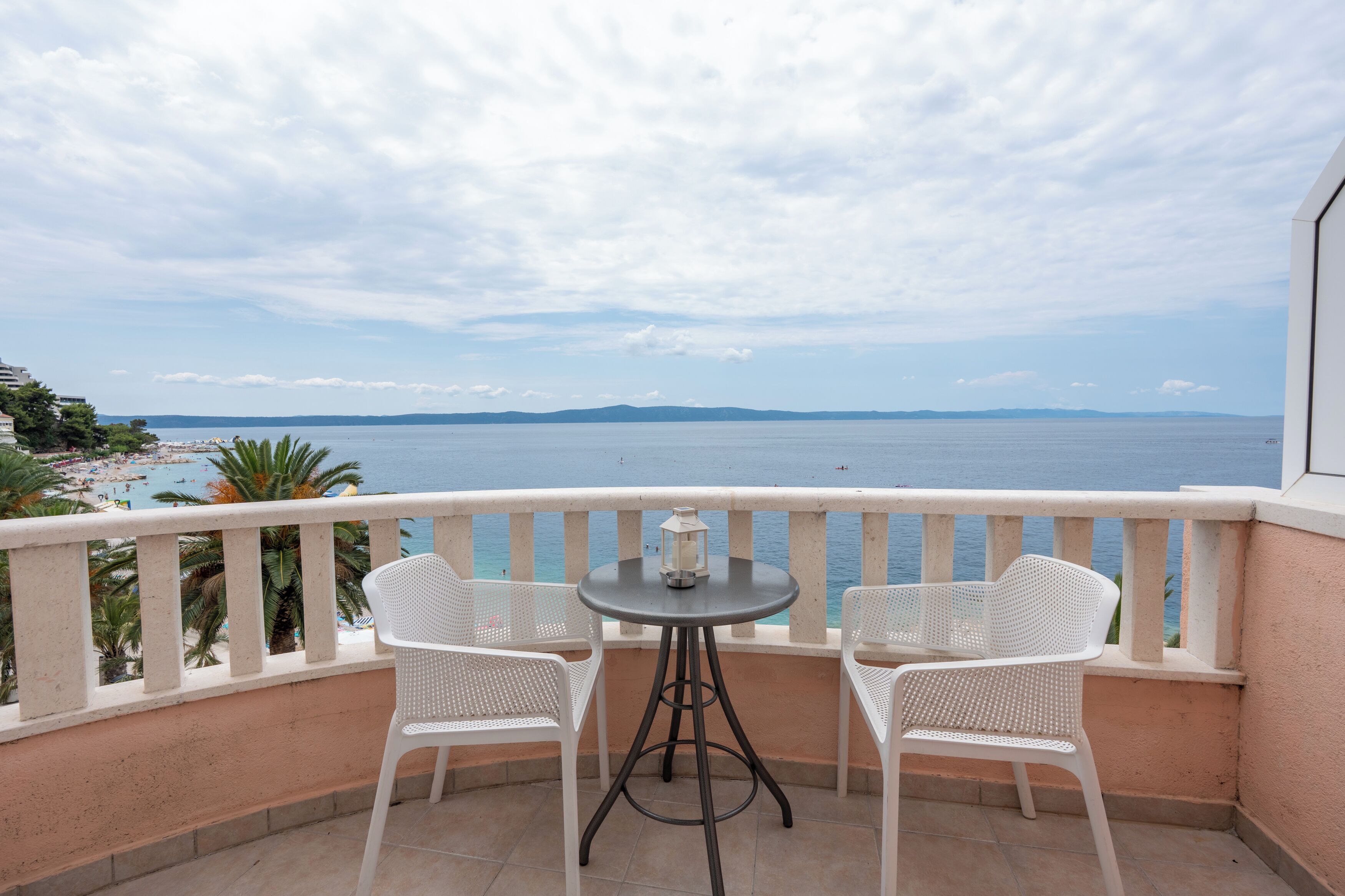 Un balcon avec deux chaises blanches et une petite table, donnant sur une plage et la mer.