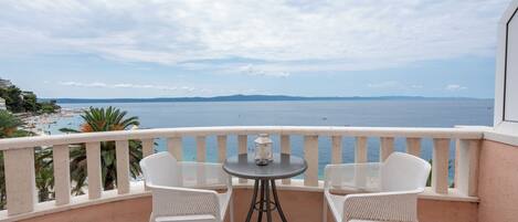 Un balcon avec deux chaises blanches et une petite table, donnant sur une plage et la mer.
