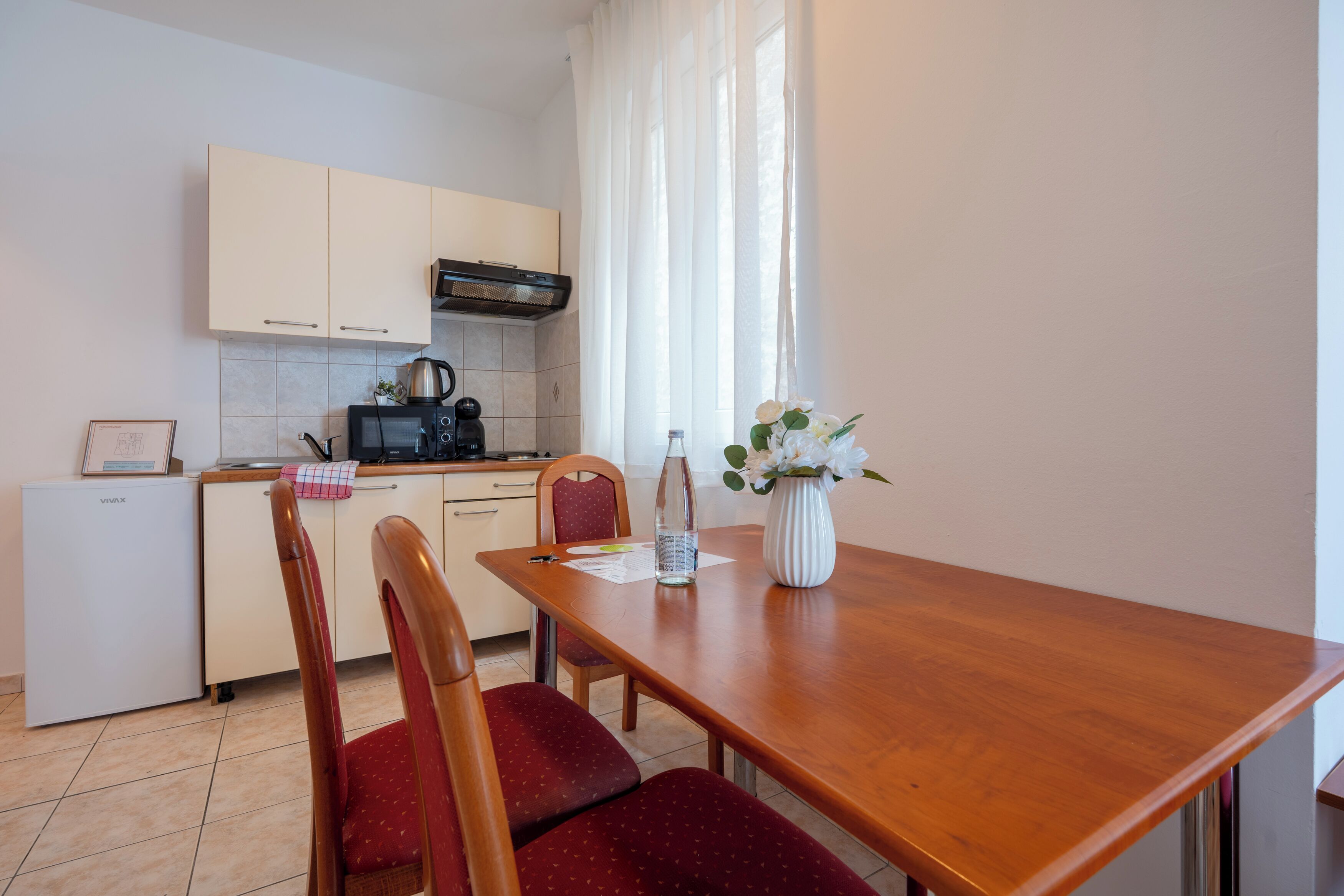 A compact kitchen with a dining table, chairs, a refrigerator, and a microwave.