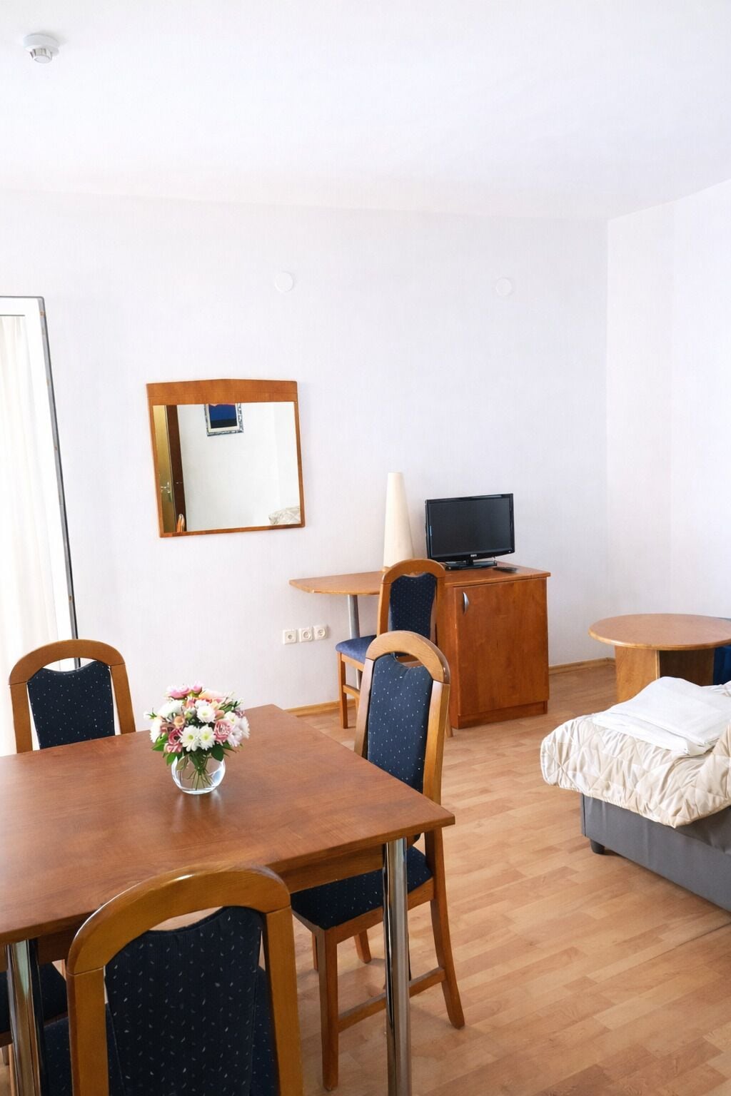 Habitación de hotel con una mesa de comedor de madera, dos sillas, un mueble bajo con televisor, una cama y un espejo en la pared.