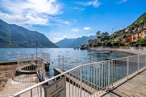 Eine Uferpromenade mit freiem Blick auf den See, eine Anlegestelle für Boote und eine gebirgige Kulisse.