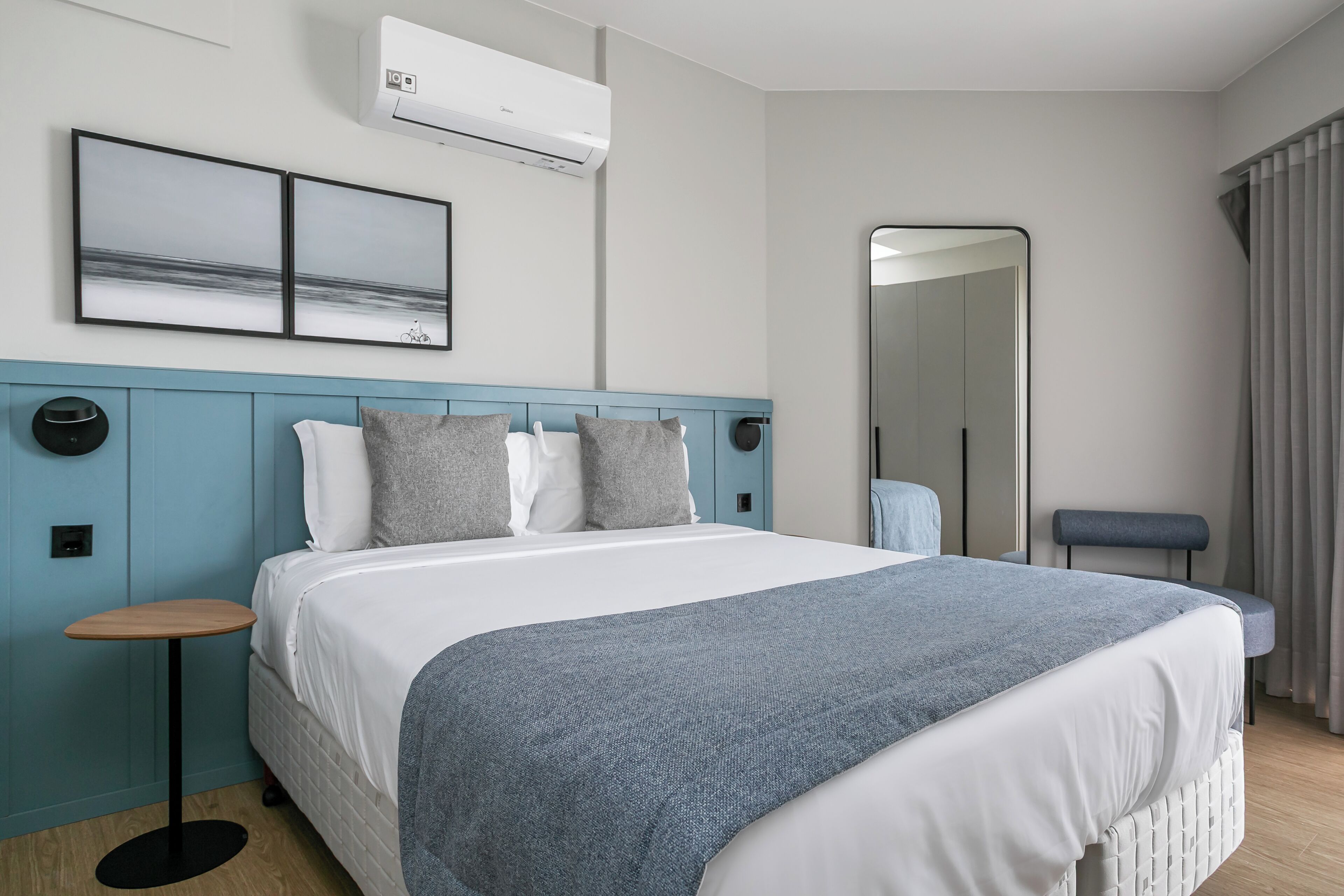 Une chambre d’hôtel moderne avec un grand lit, une table d’appoint ronde, un miroir et une vue sur la mer.