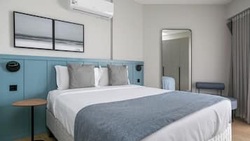 Een moderne hotelkamer met een groot bed, een rond bijzettafeltje, een spiegel en uitzicht op zee.