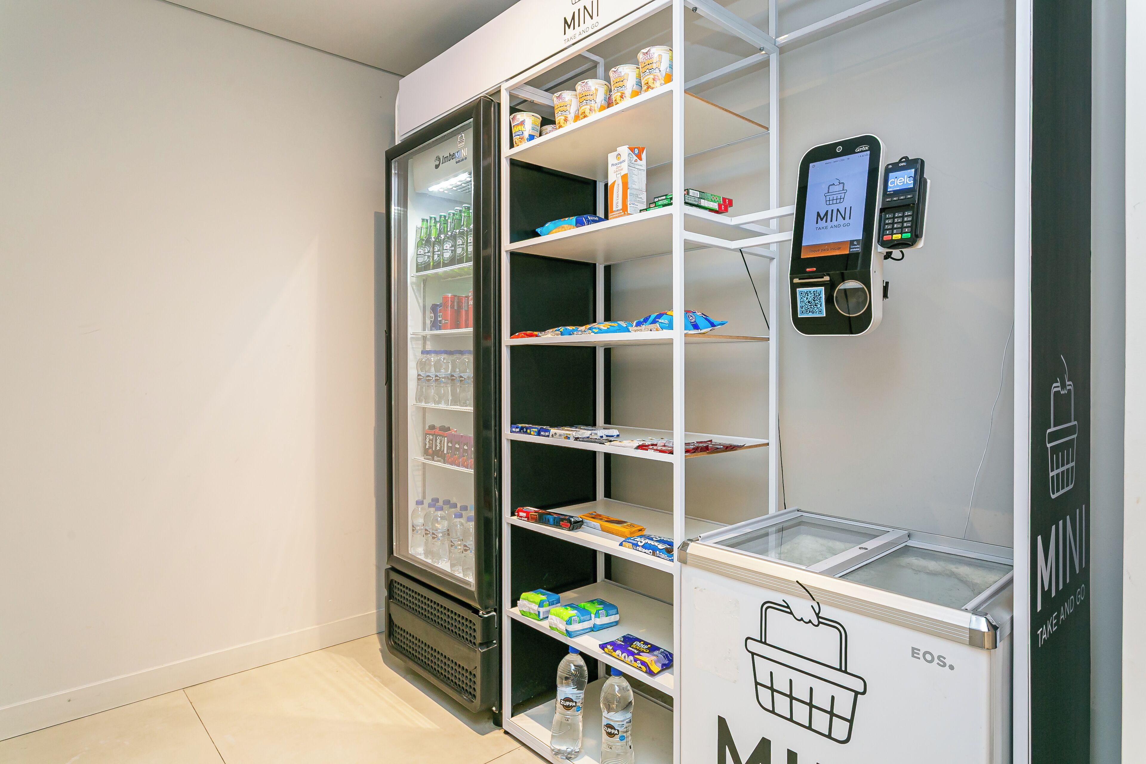 A mini fridge with shelves stocked with beverages and snacks, a mobile payment station, and a freezer compartment.