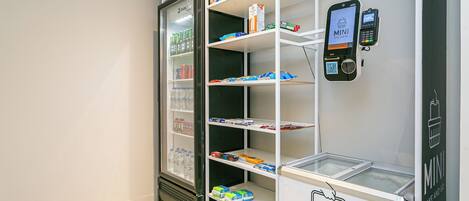 A mini fridge with shelves stocked with beverages and snacks, a mobile payment station, and a freezer compartment.