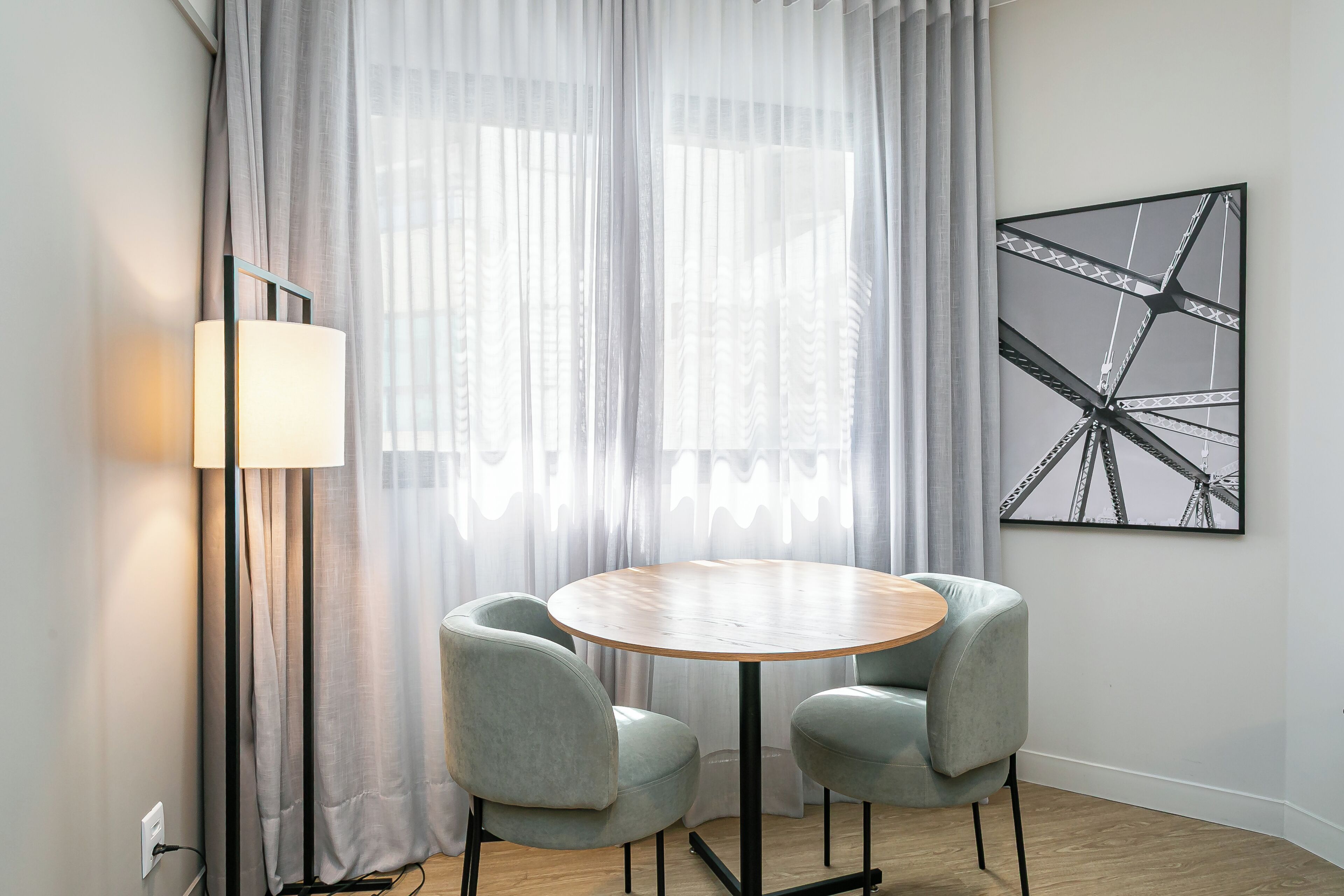A modern room with a round wooden table, two grey chairs, a floor lamp, and a large abstract painting on the wall.