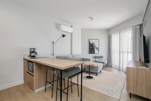 Un apartamento moderno con cocina, comedor y sala de estar. Incluye un sofá, una cafetera y un televisor.
