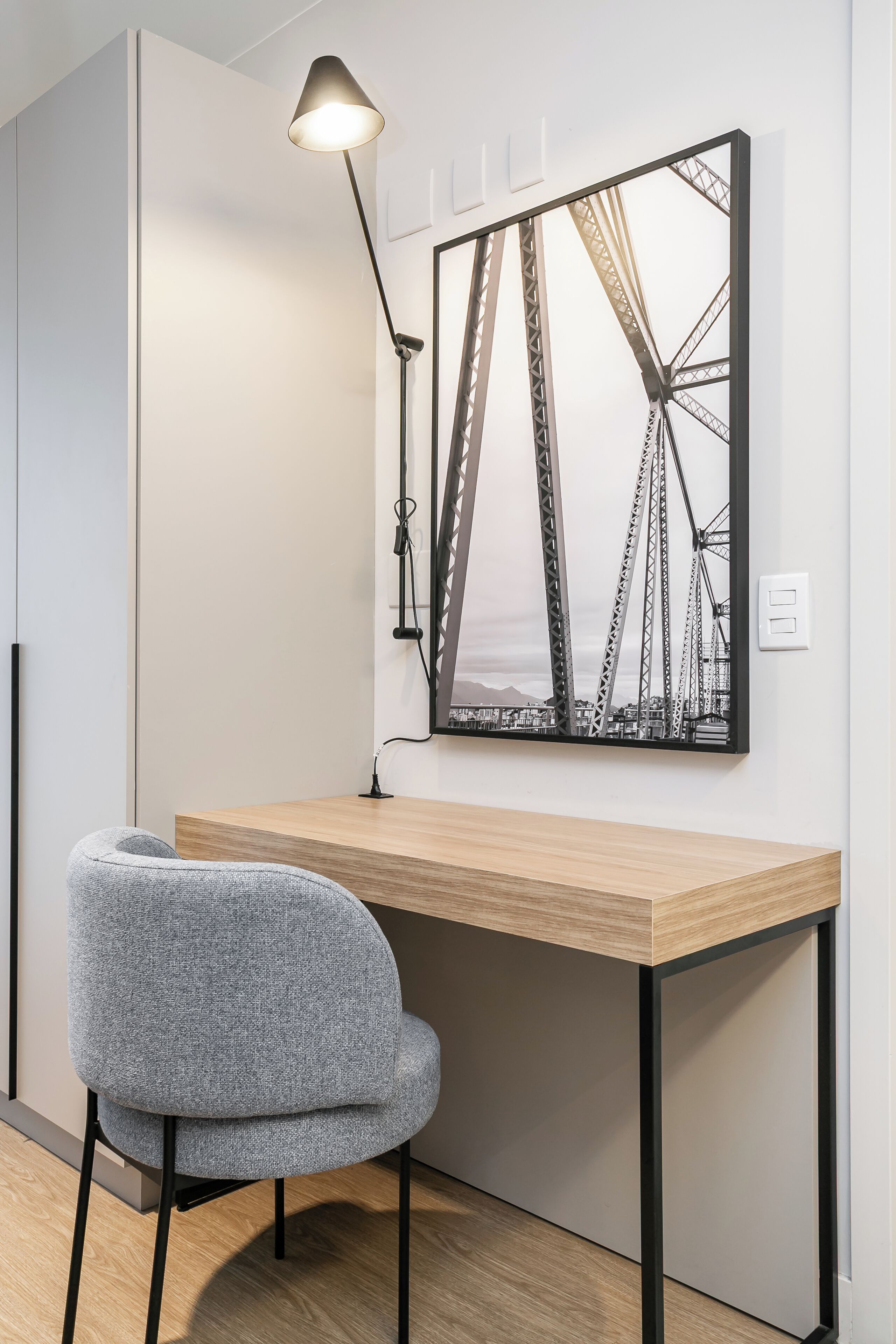 Un espacio de trabajo moderno con un escritorio de madera, una silla gris, una lámpara de pie y un cuadro con una imagen de un puente.