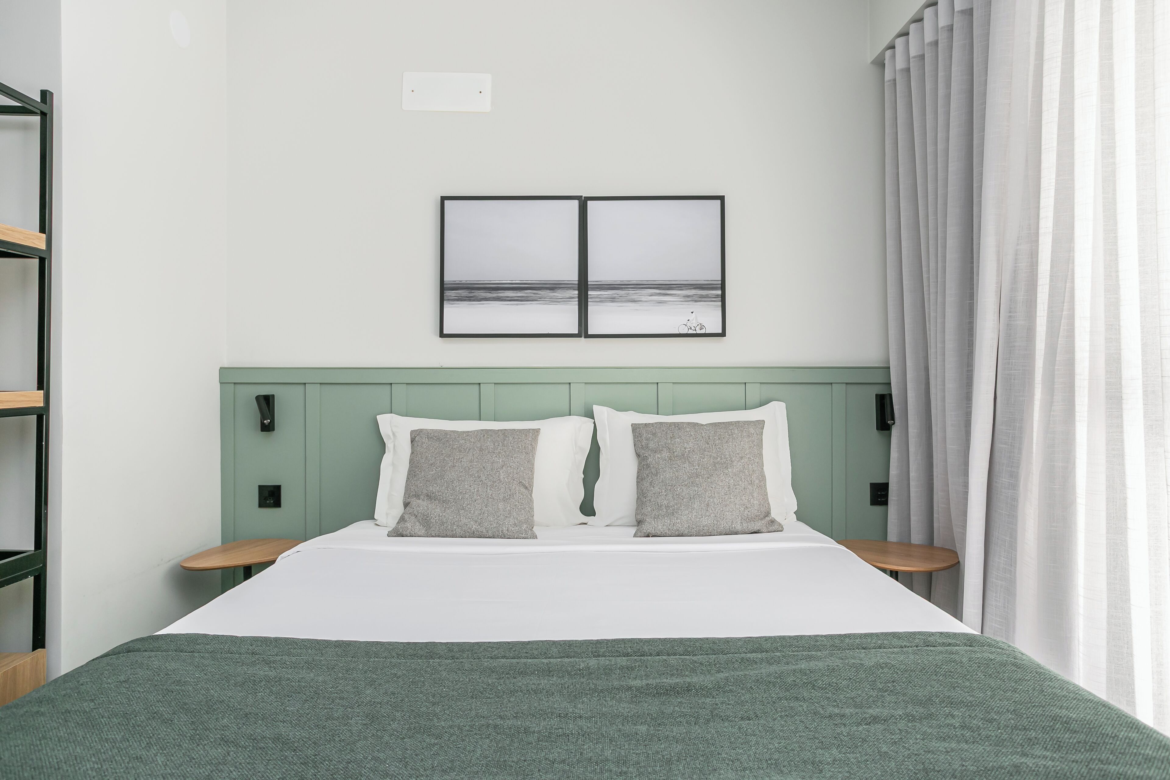 A neatly arranged hotel room with a bed, two bedside tables, a green headboard, and a framed picture on the wall.