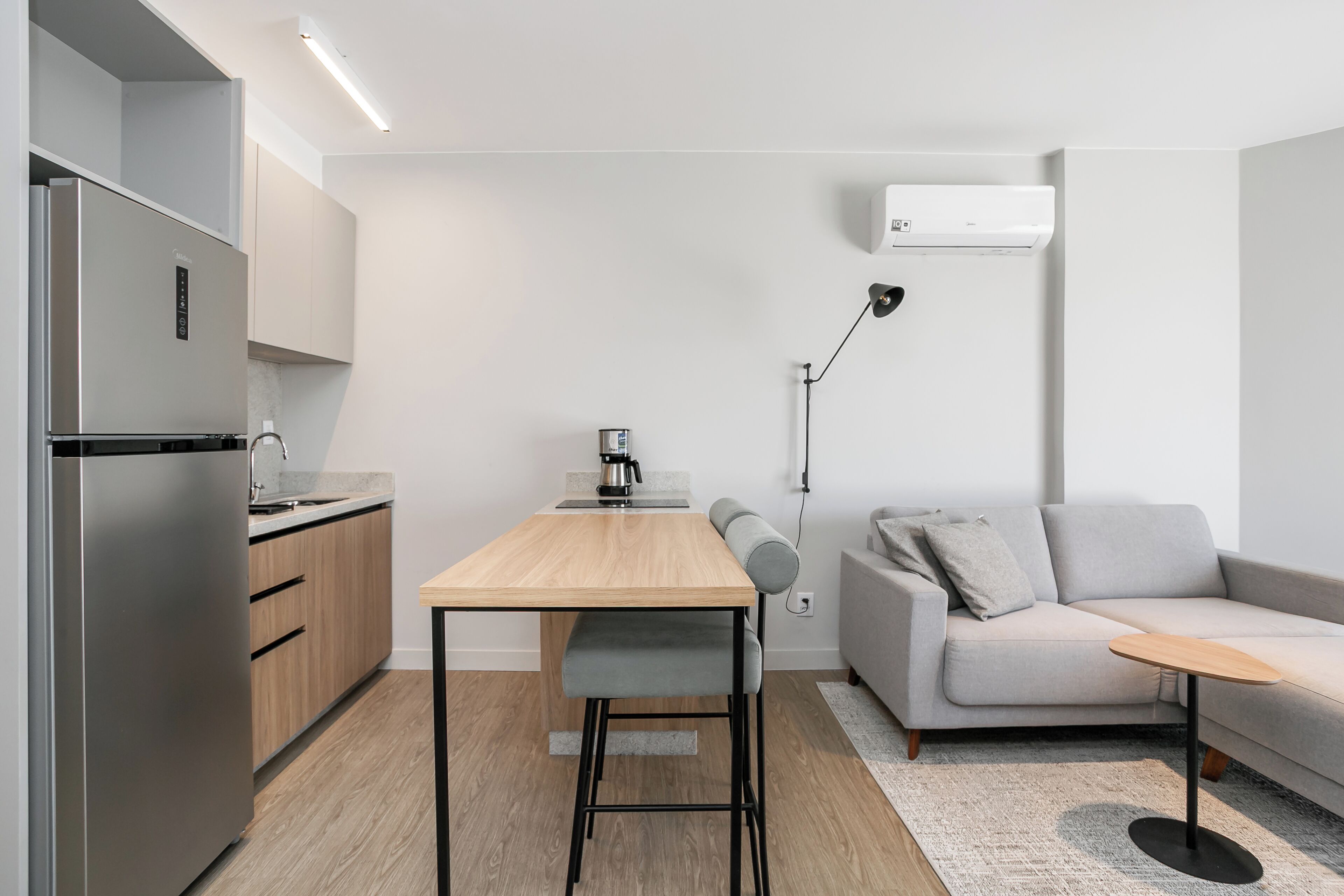 Ett modernt kök med ett inbyggt kylskåp, ett matbord med en bänk, en soffa och ett litet sidobord.
