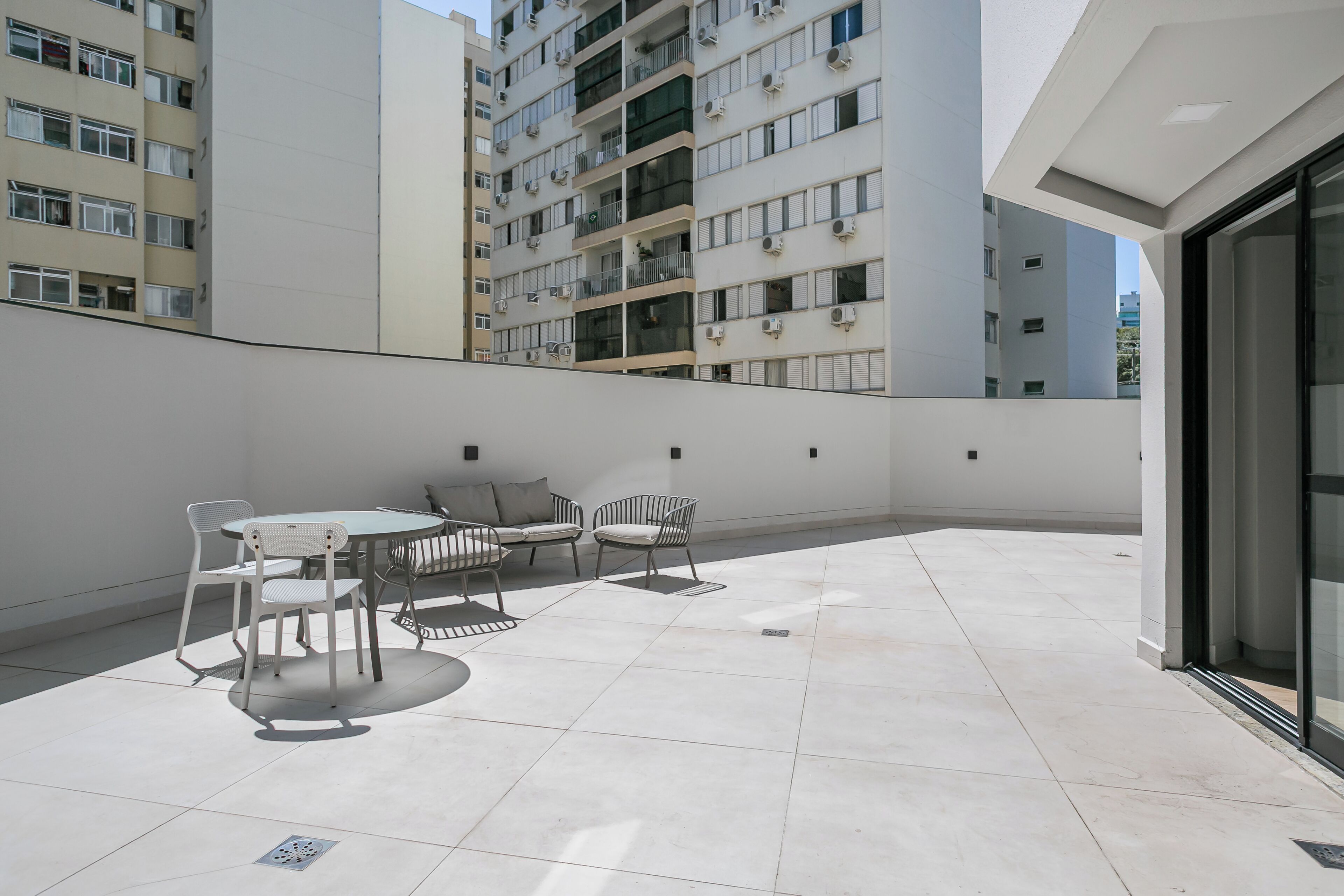 Une terrasse sur le toit, avec une table et des chaises, offrant une vue sur un immeuble de grande hauteur, et une porte vitrée donnant accès à un espace intérieur.