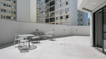 Una terrassa al terrat amb una taula i caires, vista d'un edifici alt i una porta de vidre que dona a una zona interior.