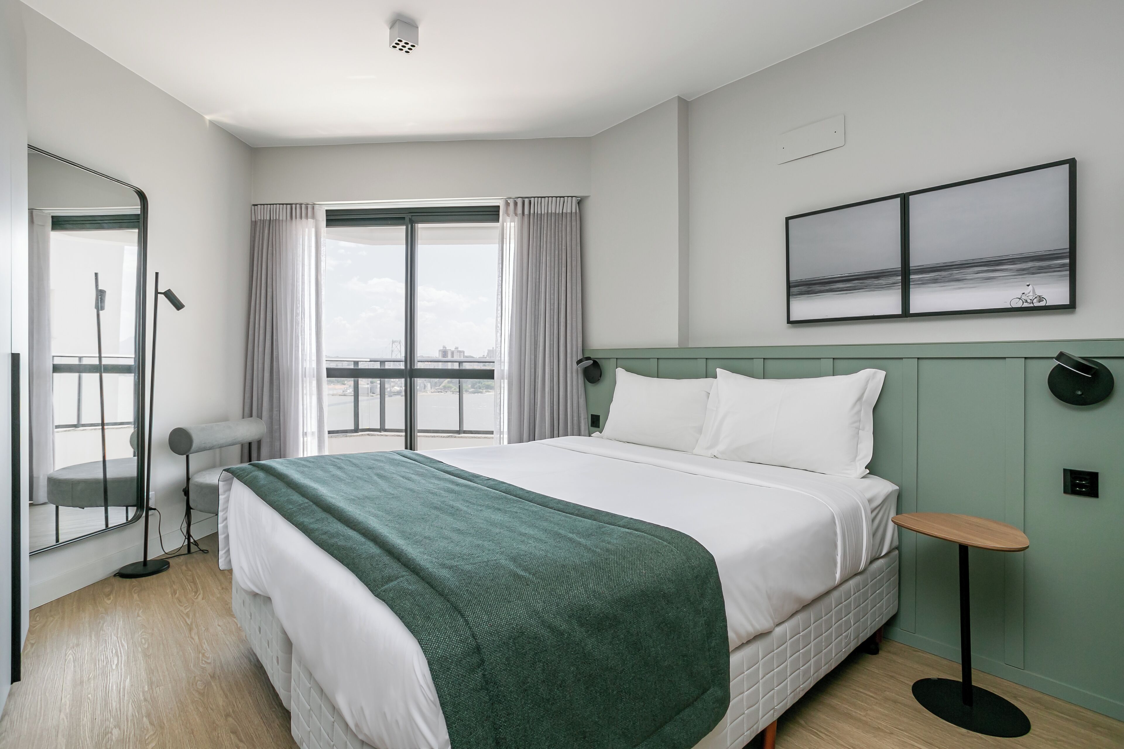 Une chambre d’hôtel avec un grand lit, une vue sur la ville par la fenêtre, une petite table et un miroir.