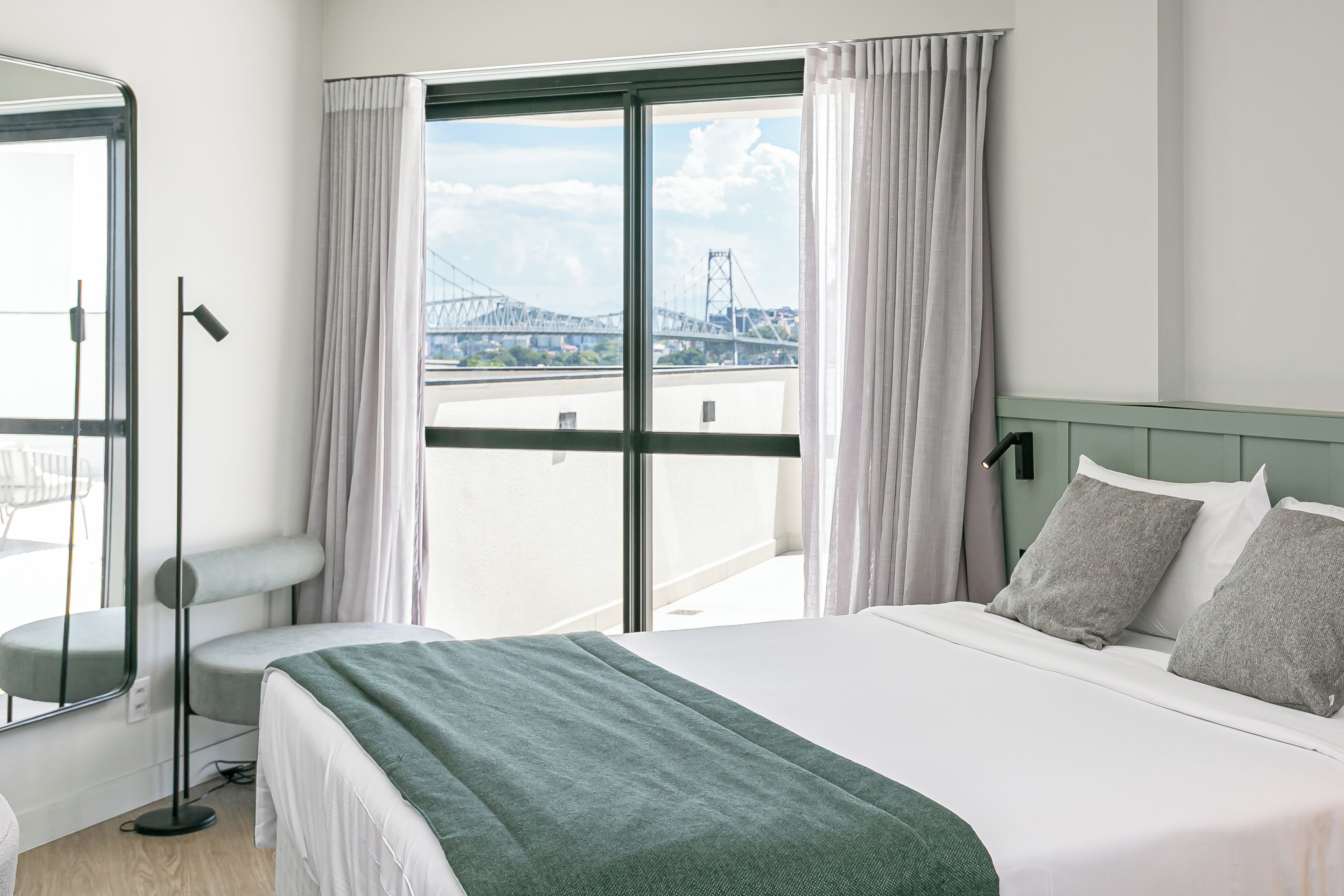 Habitación de hotel con una cama grande, vista a un puente y balcón con cortinas.