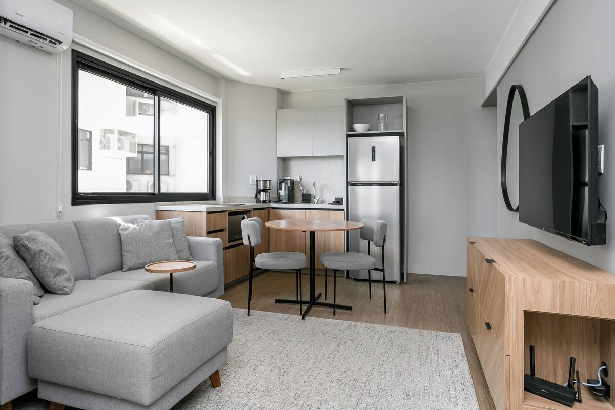 A modern kitchen with a grey sofa, a round table, and a TV mounted on the wall.