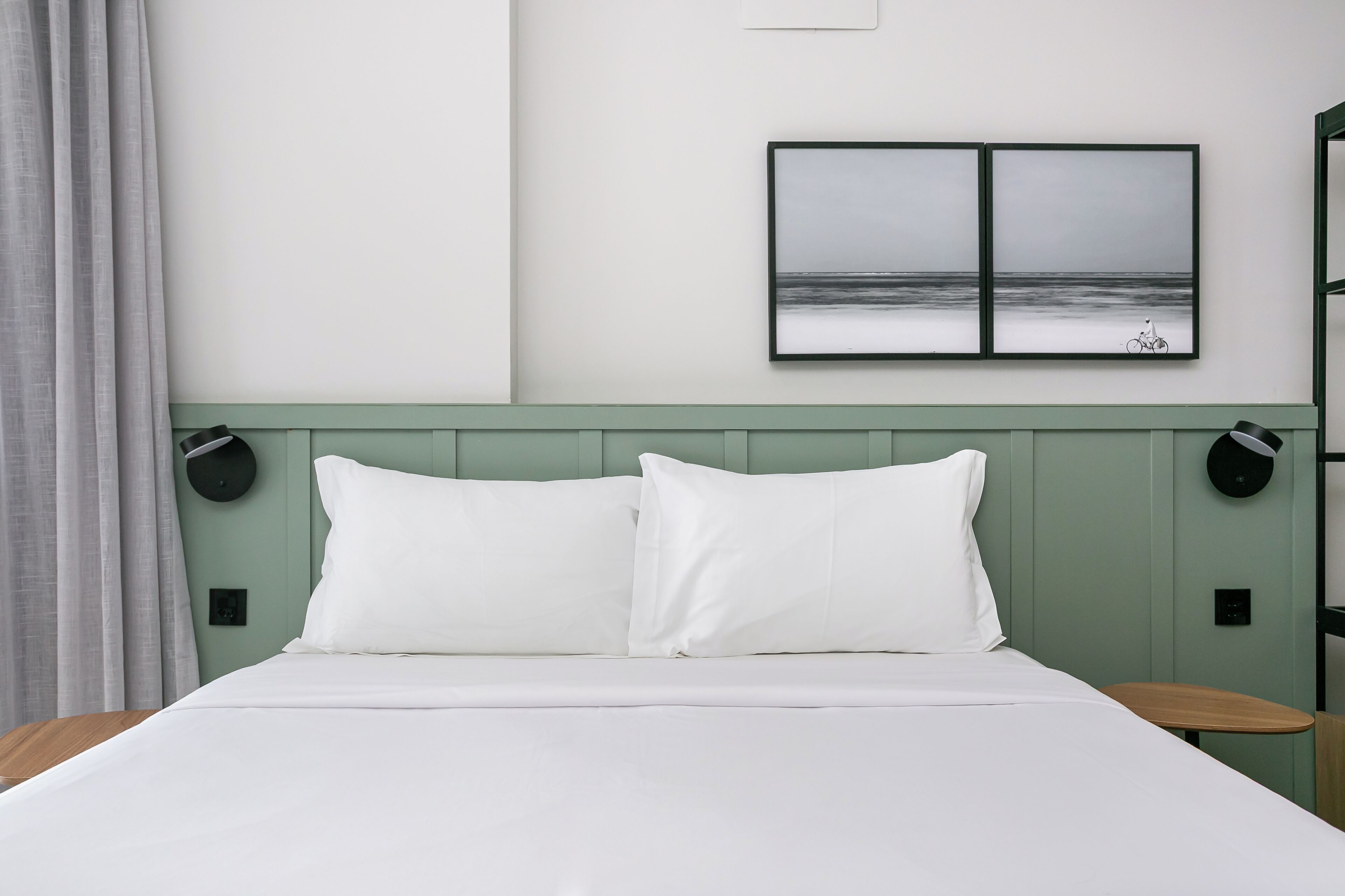 A neatly made bed with white bedding, a green headboard, and a wall-mounted picture of a beach scene.