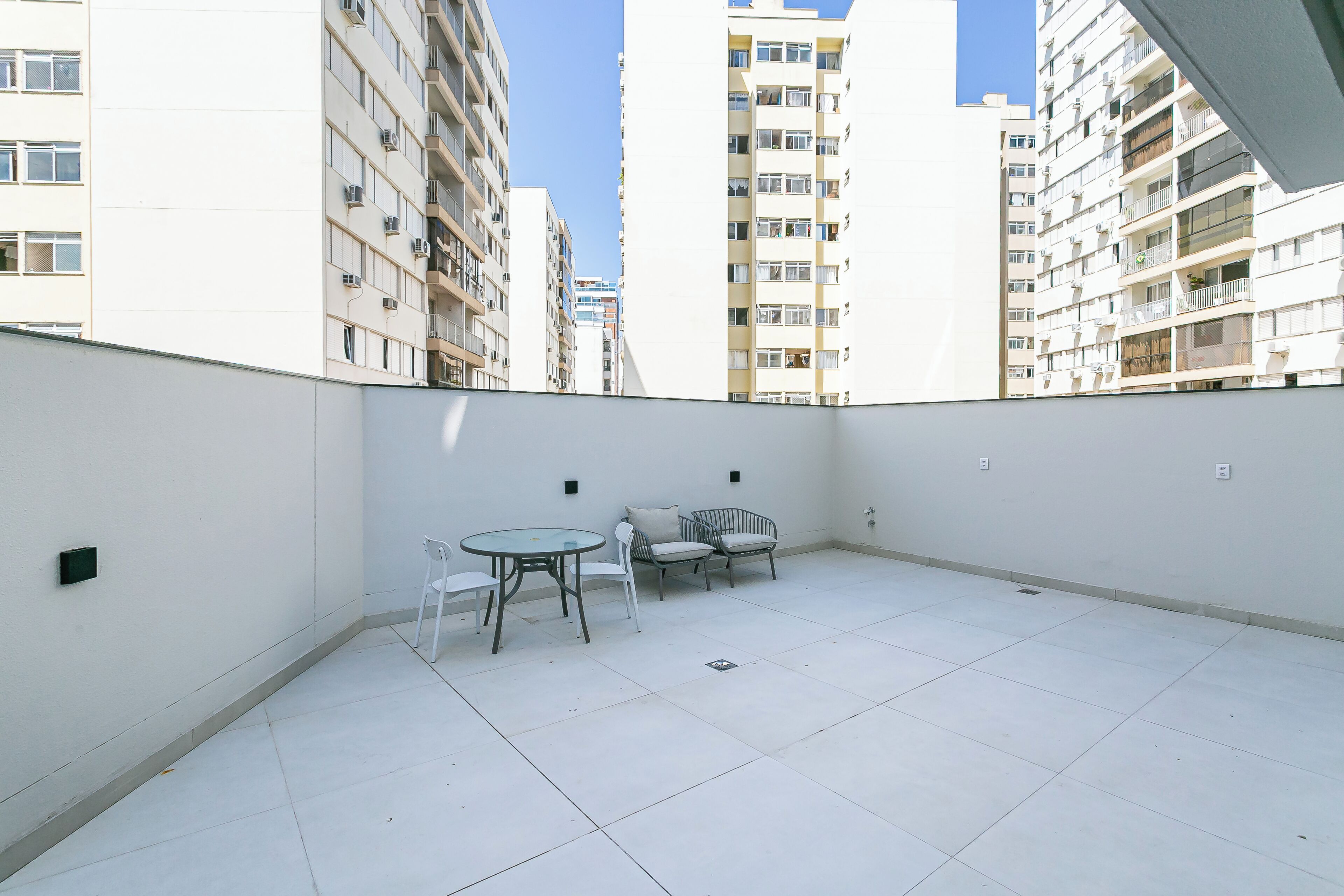 A balcony with a white tiled floor, a round glass table, and two white chairs.