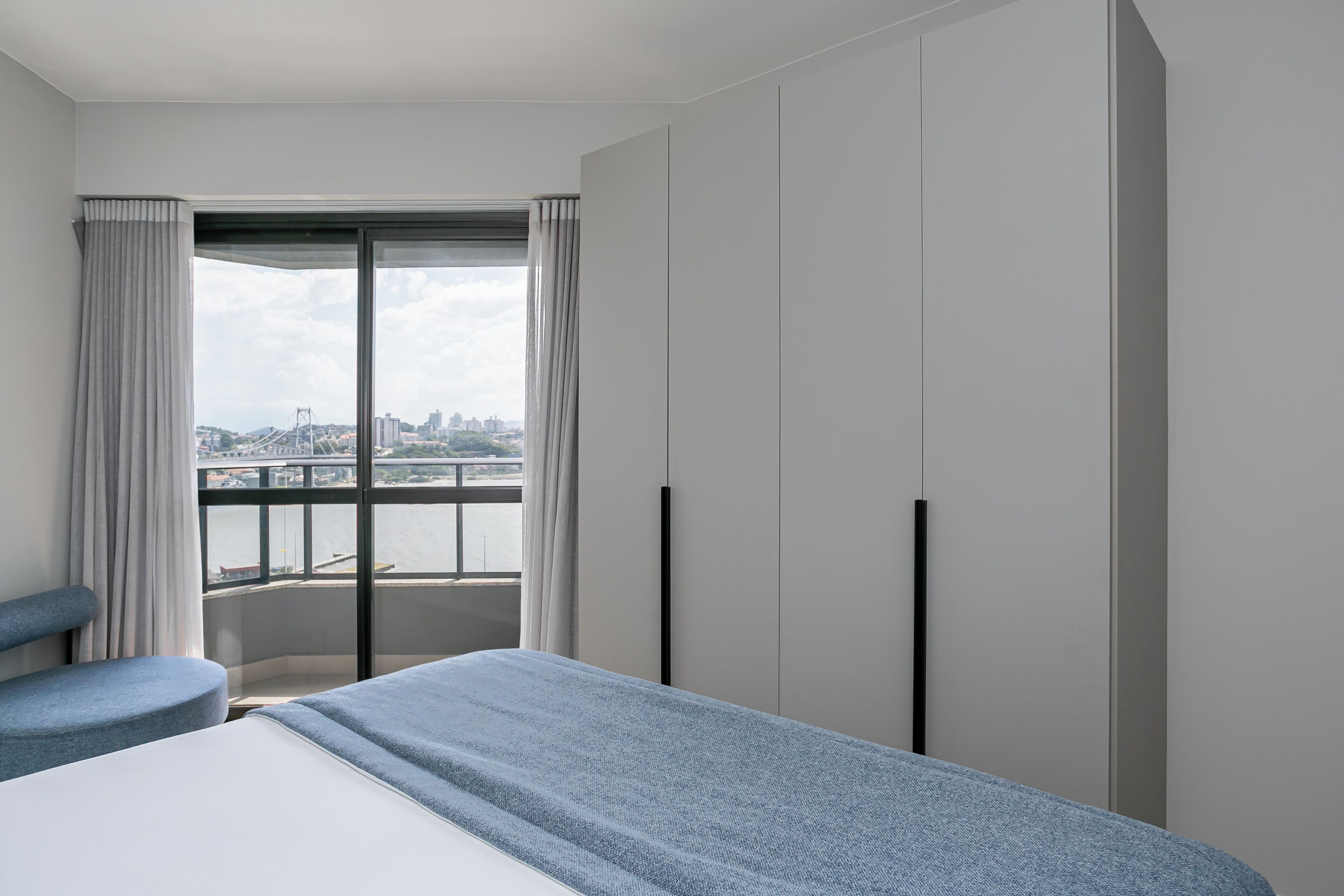 Habitación de hotel moderna con una cama grande, zona de estar y vistas a un puente y al paisaje urbano a través de un ventanal.
