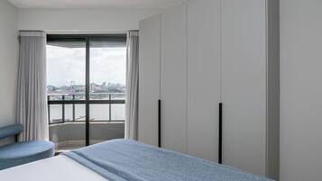 Habitación de hotel moderna con una cama grande, zona de estar y vistas a un puente y al paisaje urbano a través de un ventanal.