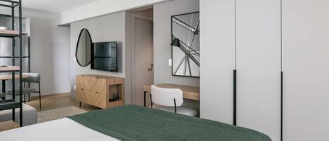 A modern bedroom with a bed, a desk, a chair, a TV, and a large mirror.