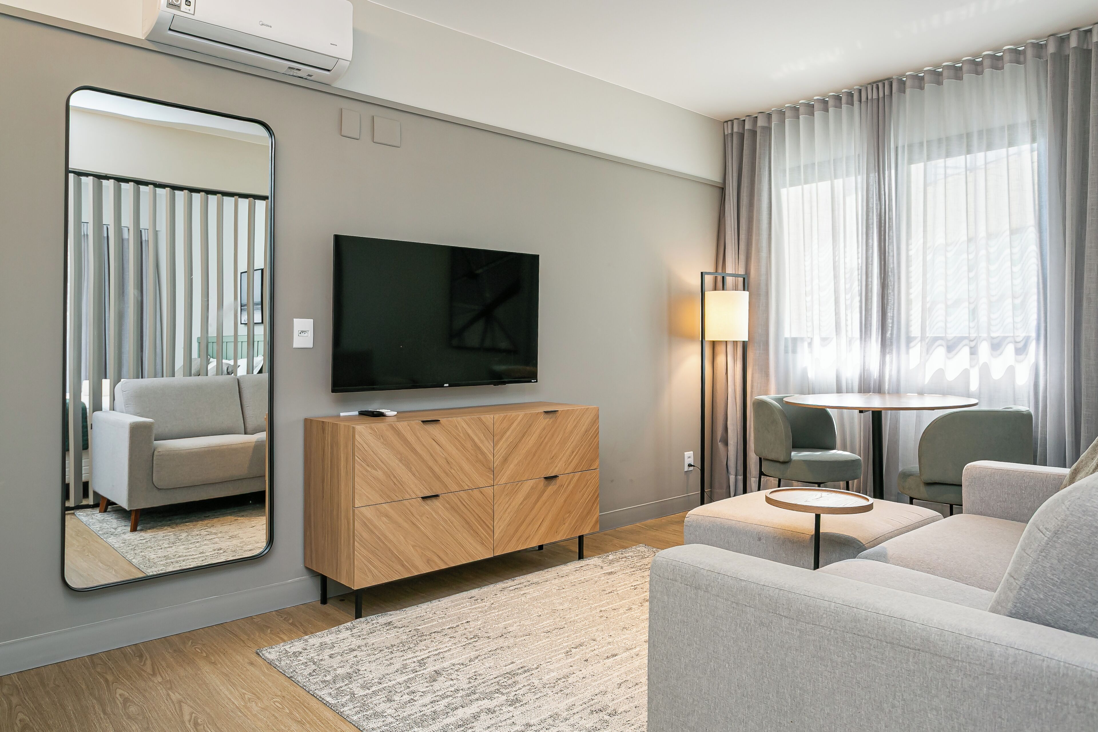 Una sala moderna con un televisor de pantalla plana, un mueble de madera, una mesa redonda de centro y un sofá.