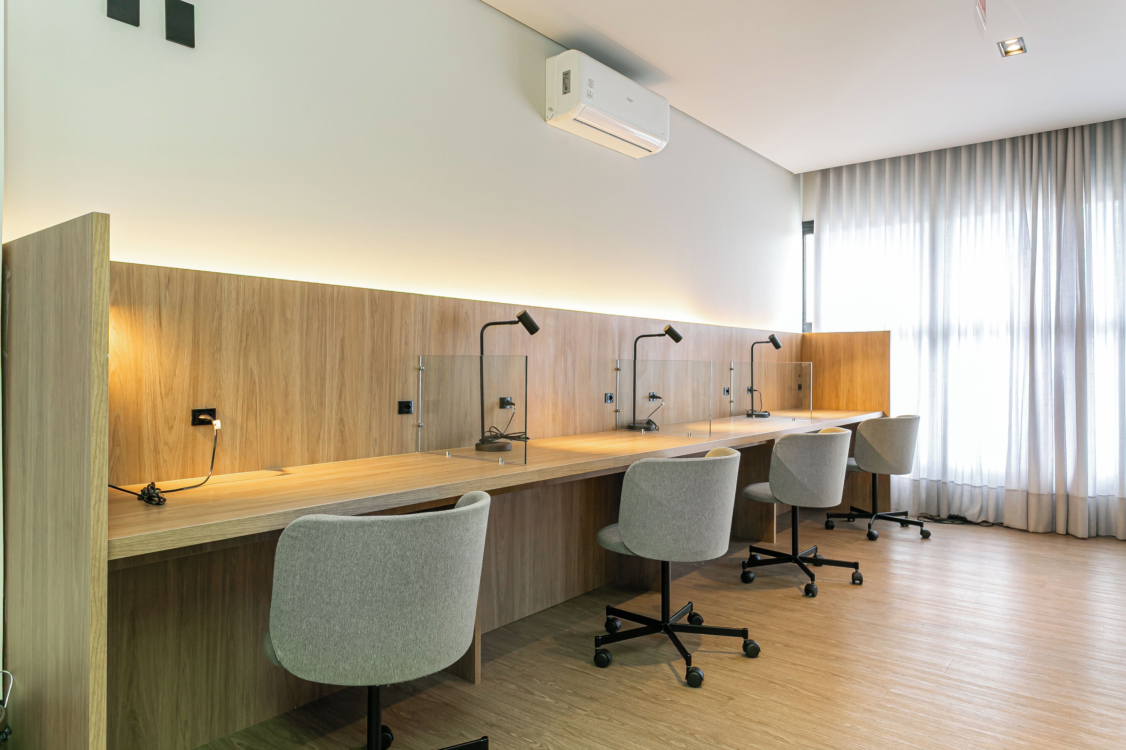 Ein moderner Büroraum mit einem langen Holztisch, drei grauen Bürostühlen und einer Decken-Klimaanlage.