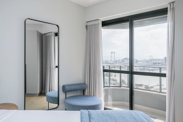 Une chambre d’hôtel moderne avec une grande fenêtre, un fauteuil rond bleu, un lit et un miroir.