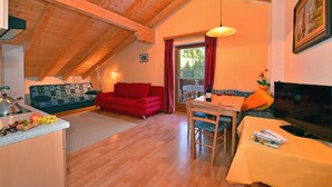 Une pièce chaleureuse de style loft, avec un plafond en bois, un canapé rouge, une table à manger avec des chaises, une télévision et un coin cuisine équipé d’une bouilloire et de fruits.