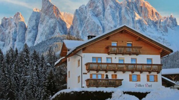 Un chalet de montagne à la façade en bois, doté de balcons et offrant une vue sur des sommets enneigés.