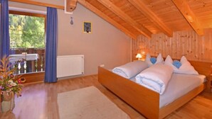 Une chambre avec un plafond en bois, un grand lit, une fenêtre avec des rideaux et une vue sur les arbres à l’extérieur.