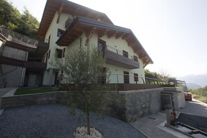 Un bâtiment à deux étages doté d’un balcon, d’un mur en pierre et d’un petit arbre au premier plan.