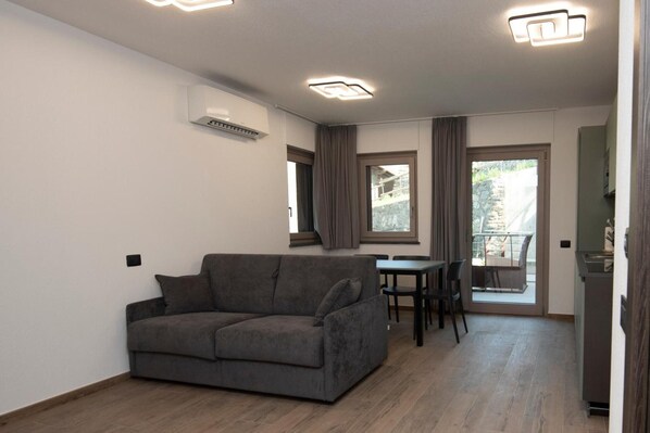 Un salon moderne avec un canapé gris, une table à manger avec des chaises et un coin cuisine.