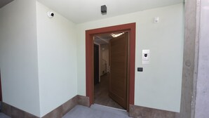 A hallway with a wooden door, a light switch, and a smoke detector on the wall. - Suly Apartments 5 - cir0086 (Cillian)