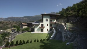 A multi-story building with a sloped roof, a fenced yard, and a mountainous backdrop. - Suly Apartments 5 - cir0086 (Cillian)