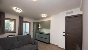 A modern living room with a grey sofa, a kitchen with green cabinets, and a wooden door. - Suly Apartments 5 - cir0086 (Cillian)