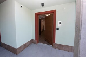 Un corridoio con una porta in legno, un interruttore della luce e un rilevatore di fumo sul muro.