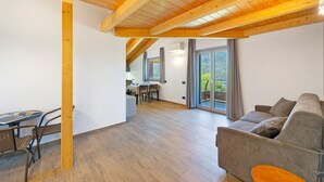 A spacious living area with a wooden ceiling, a sofa, a dining table with chairs, and a view through large glass doors. - Suly Apartments 3 – Modern Accessible Stay with Mountain Views in Saint-Vincent (Cillian)