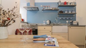 A kitchen with a wooden table, two wine glasses, a book, and a vase with dried flowers. - The Old Studio (Penzance)
