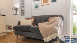 A cozy living room with a grey sofa, a white fluffy rug, and a coffee table with blue and white striped cups. - The Old Studio (Penzance)