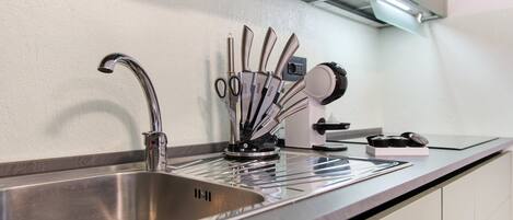 Un évier de cuisine en acier inoxydable, doté d’un robinet moderne, un bloc à couteaux contenant différents types de couteaux et une machine à café posée sur le plan de travail.