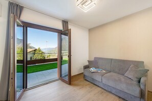 Una habitación con puerta corrediza de vidrio que da a un balcón, un sofá gris con un libro y una lámpara moderna.