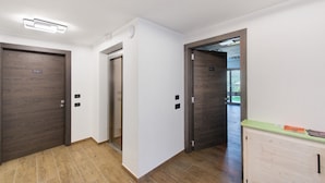 A hallway with wooden doors, a light switch, and a thermostat on the wall. - Suly Apartments 1 - cir0082 (Cillian)