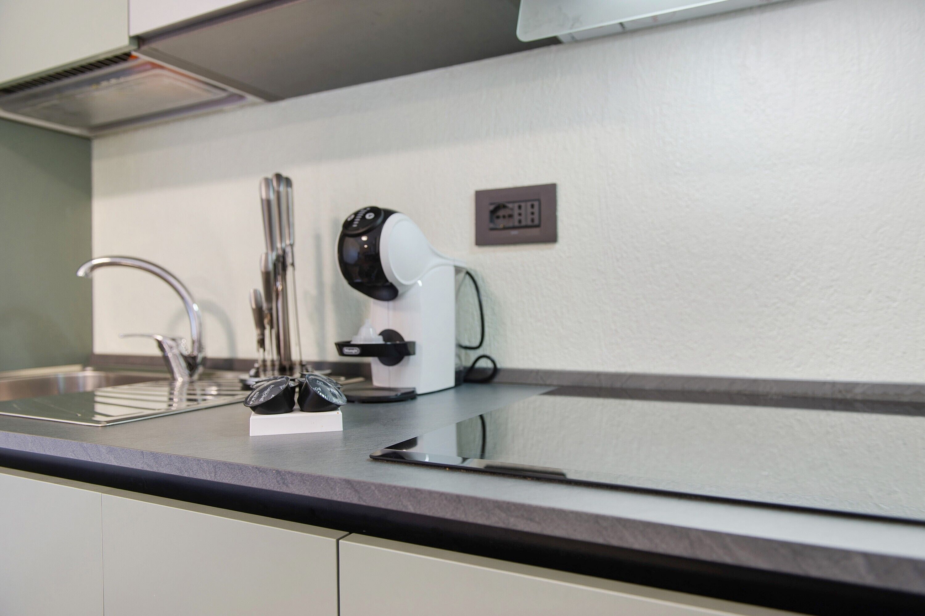 A modern kitchen with a stainless steel sink, a coffee machine, and a power outlet on the wall.